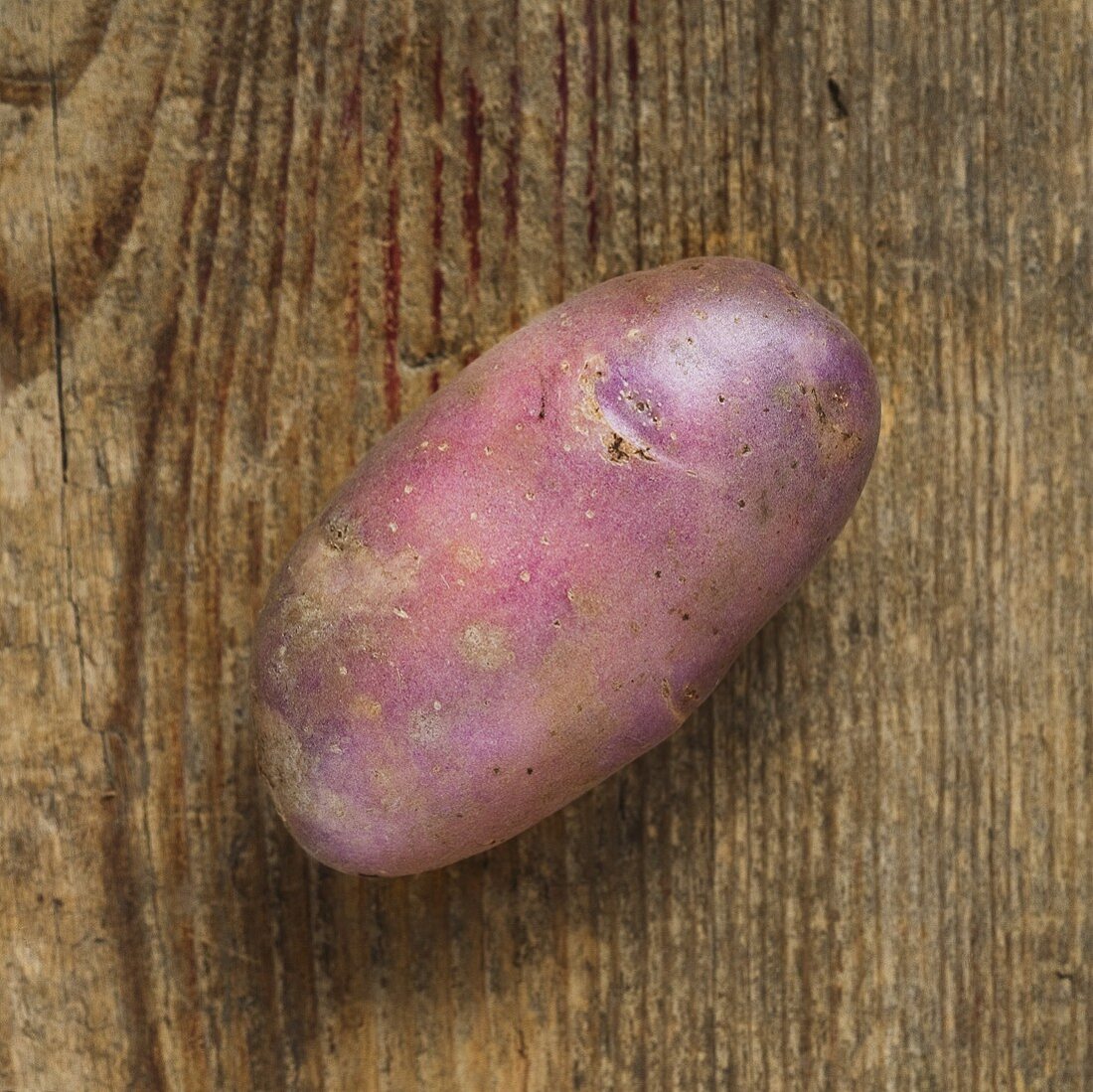 Eine violette Kartoffel auf Holzuntergrund