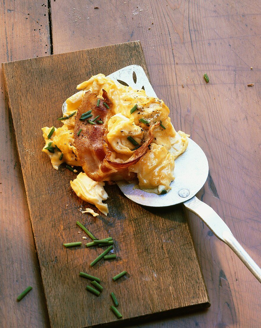 Scrambled egg with bacon and chives on wooden board