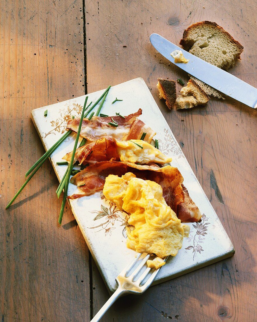 Scrambled egg with bacon and chives on porcelain board