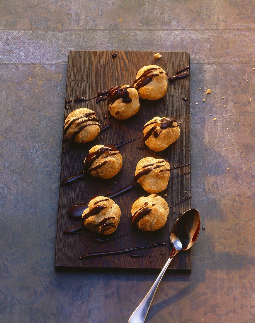 Profiteroles mit Schokoglasur auf Holzbrett