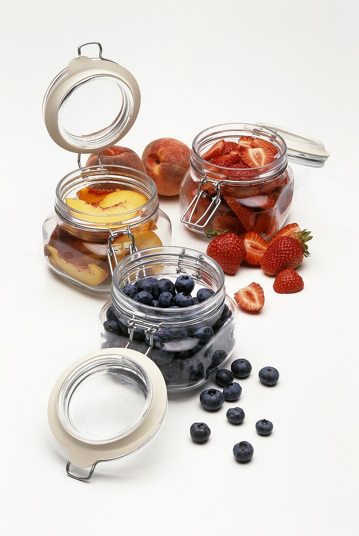Blueberries, peaches and strawberries in preserving jars