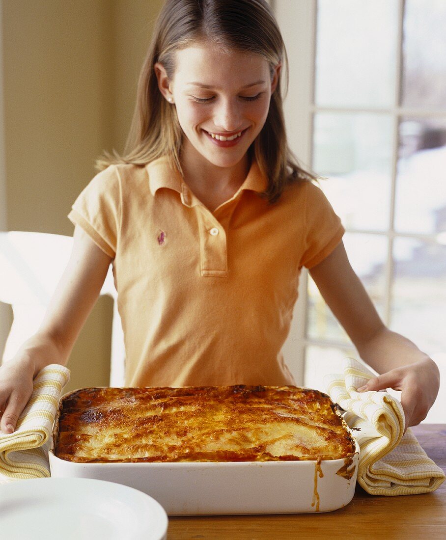 Girl holding vegetable lasagne in baking dish