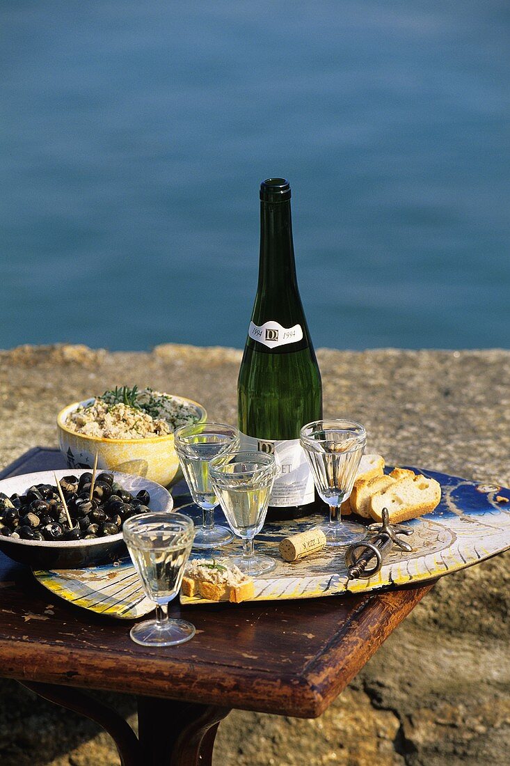 Sekt, Oliven & Brot mit Fischcreme auf Tisch am Meer