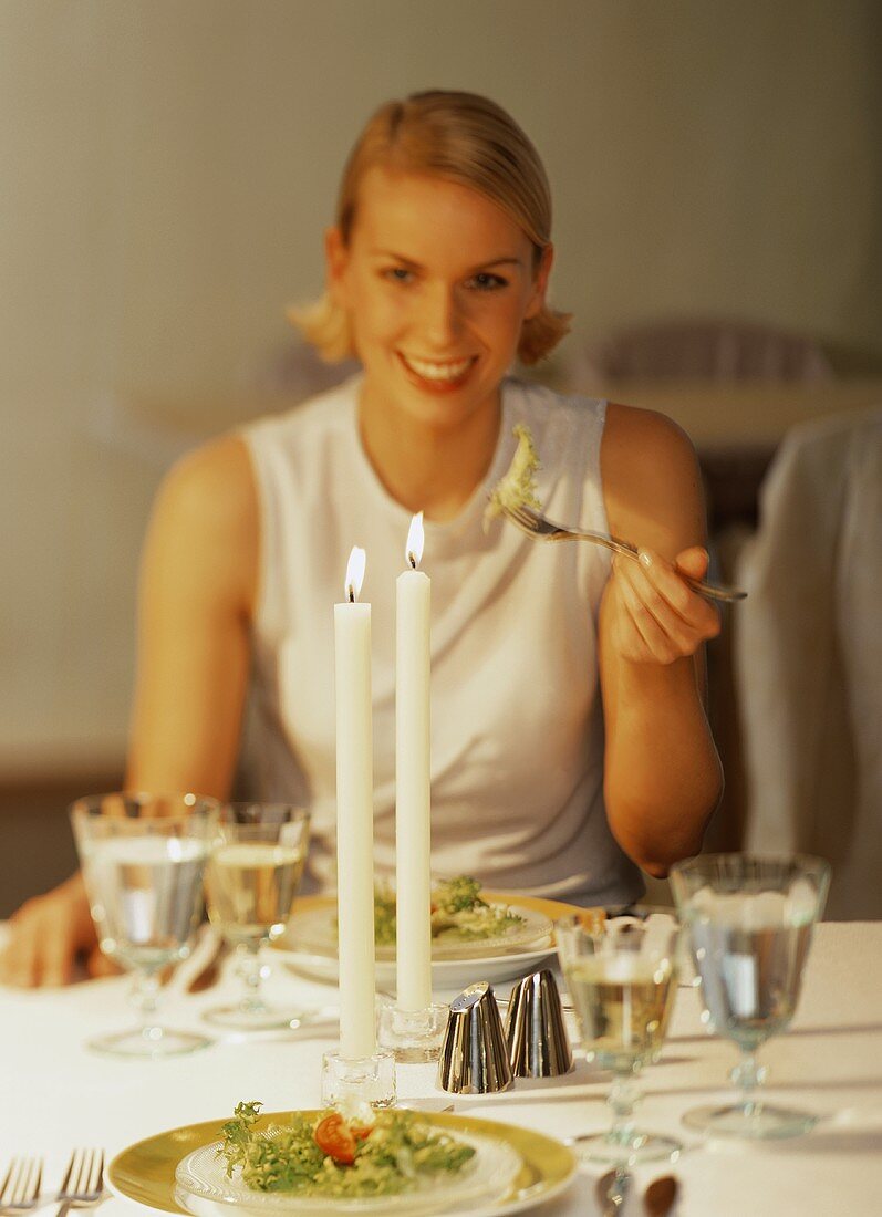 Junge Frau isst Salat am festlich gedeckten Tisch