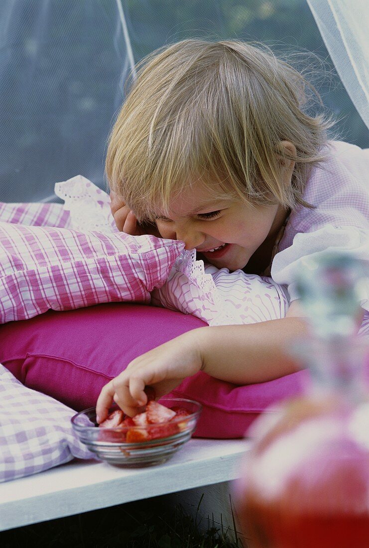 Kleines Mädchen greift in eine Schale mit Erdbeeren