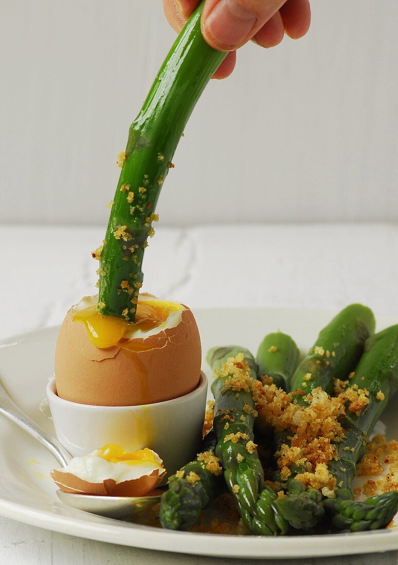 An asparagus spear being dipped into a soft egg