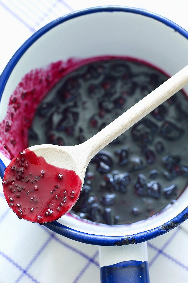 Blackcurrant jam in an enamel pot with a wooden spoon