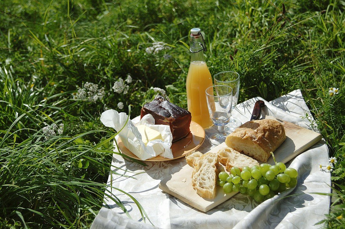 Picknick mit Schinken, Butter, Ciabatta, Trauben und Saft