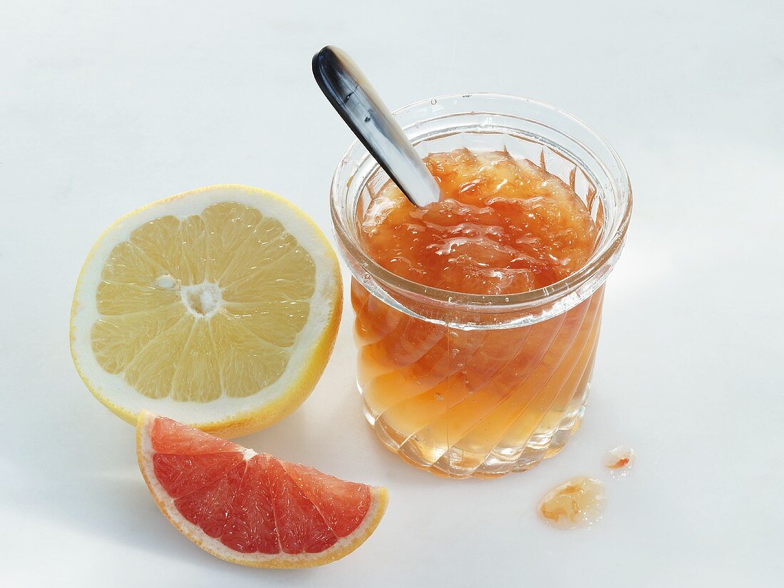 A jar of grapefruit jam with a pink and a yellow grapefruit to the side