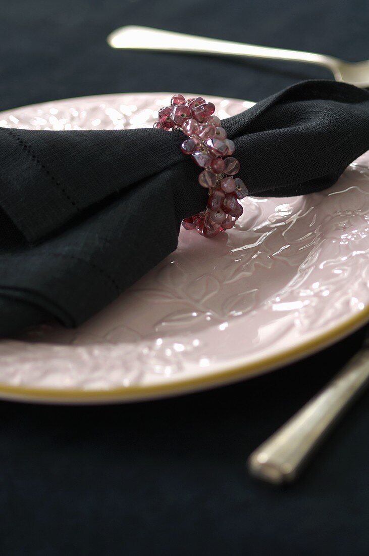 A napkin with a napkin ring on a pink plate