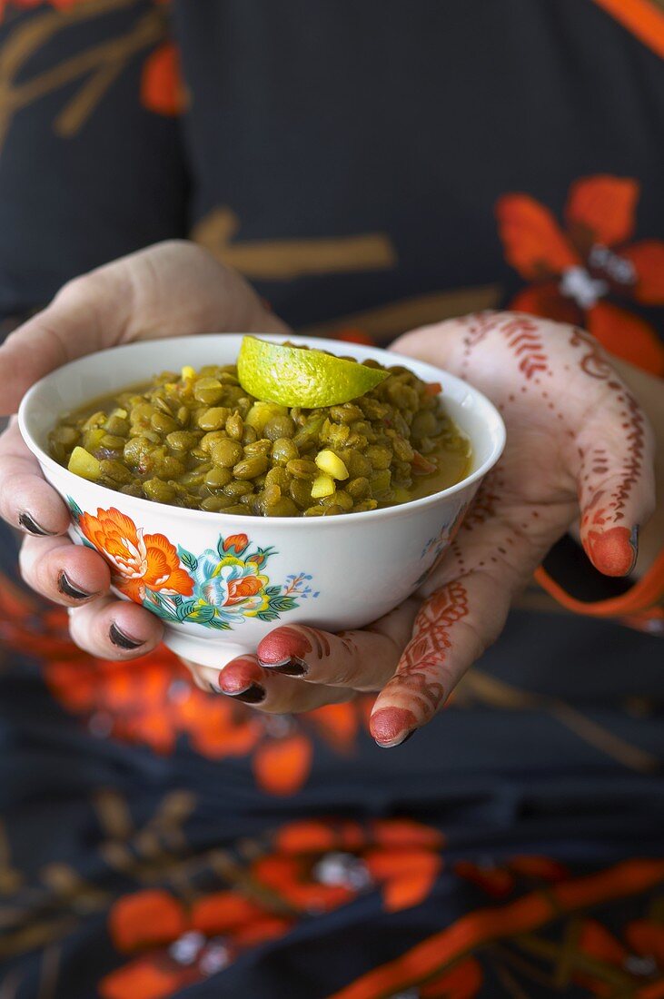 Henna-painted hands holding a bowl of lentils