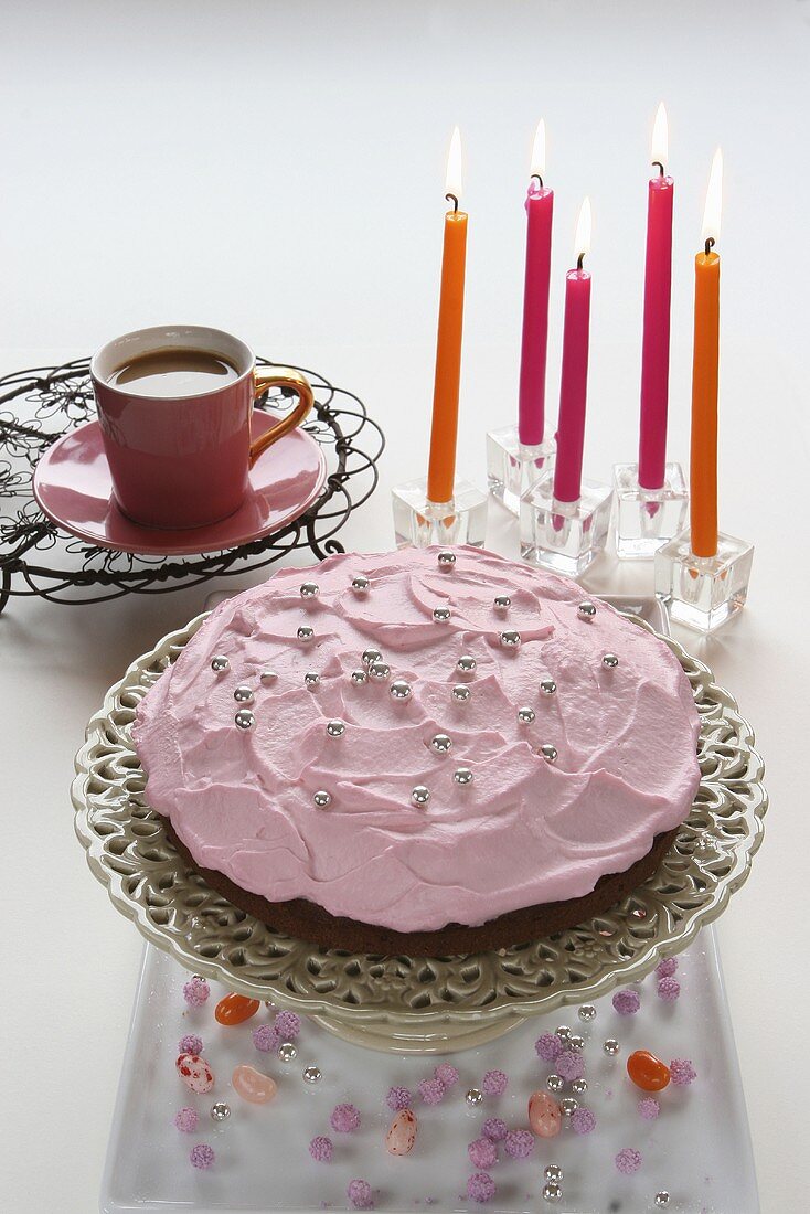 Raspberry cream cake with silver balls with candles and coffee in the background