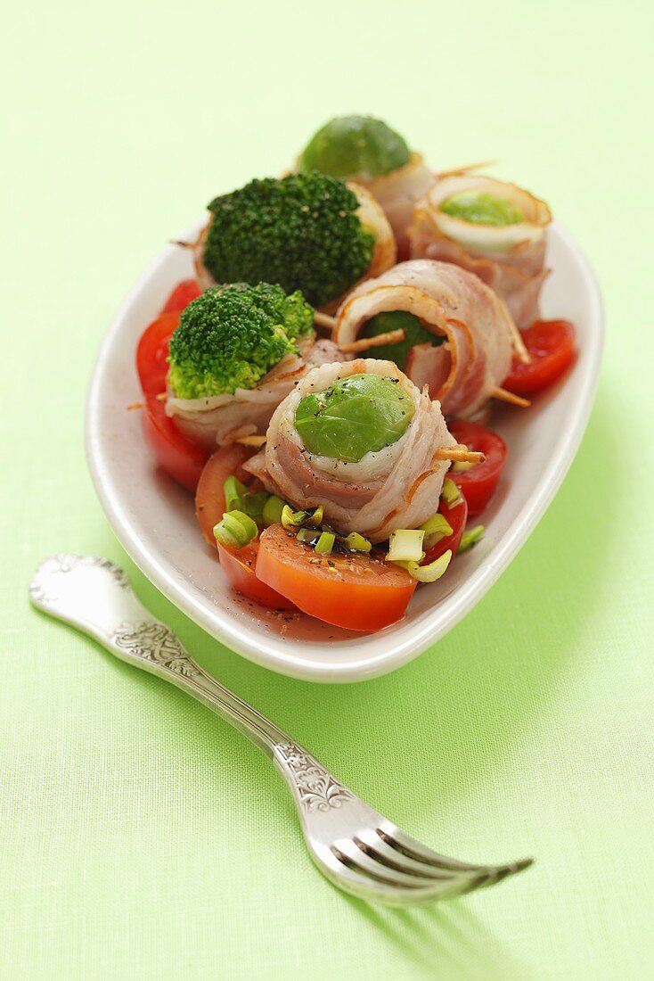 Brussels and broccoli florets wrapped in bacon with a tomato salad