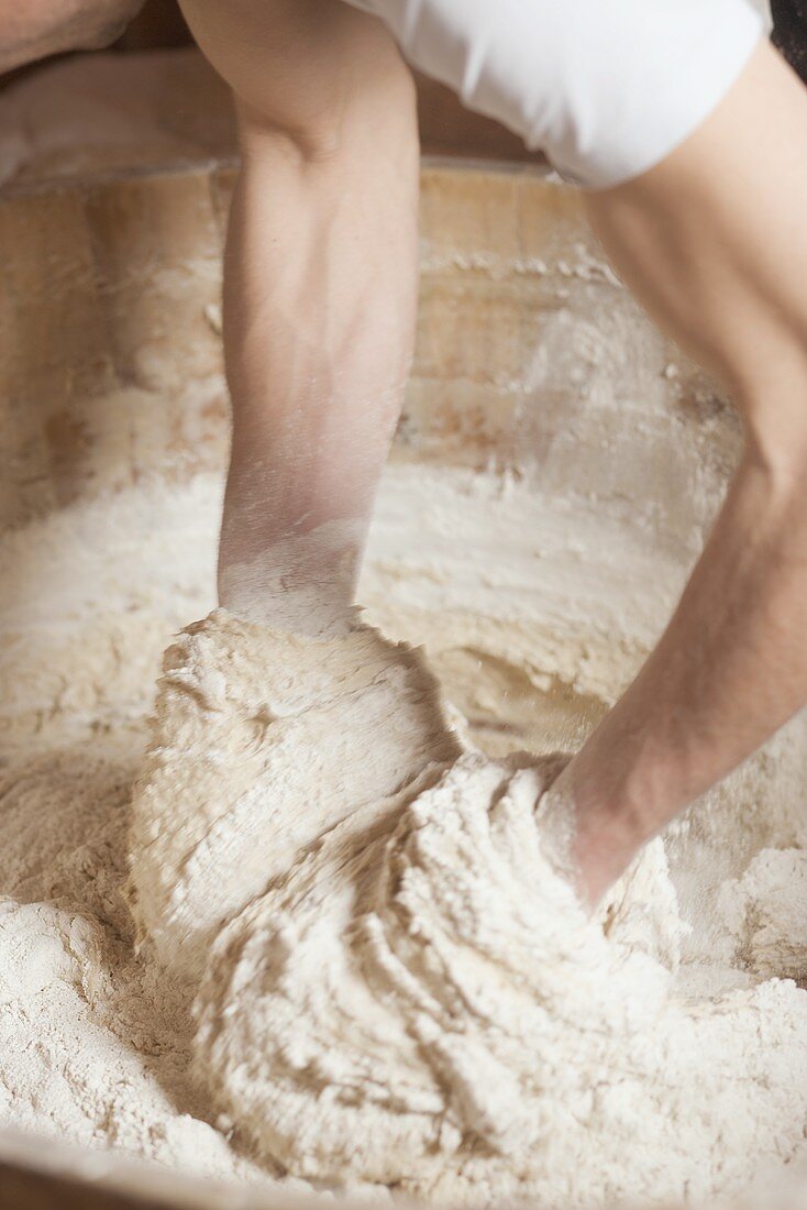 Baker kneading dough in a wooden tub