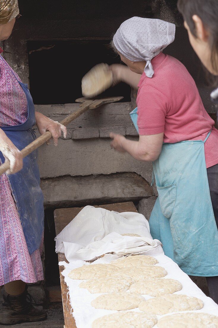 Countrywomen putting unbaked bread into old stone oven