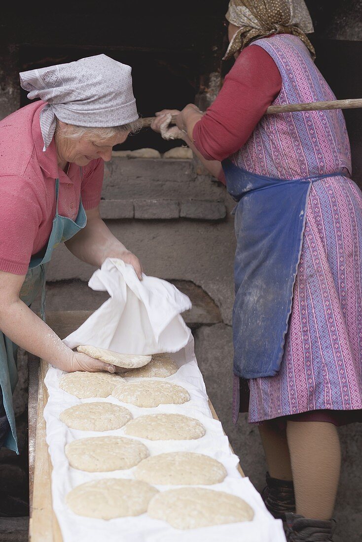 Countrywomen putting unbaked bread into old stone oven