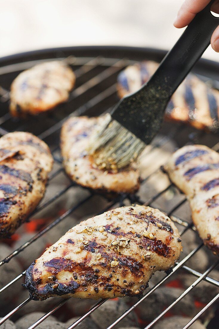 Chicken breasts on barbecue being brushed with marinade