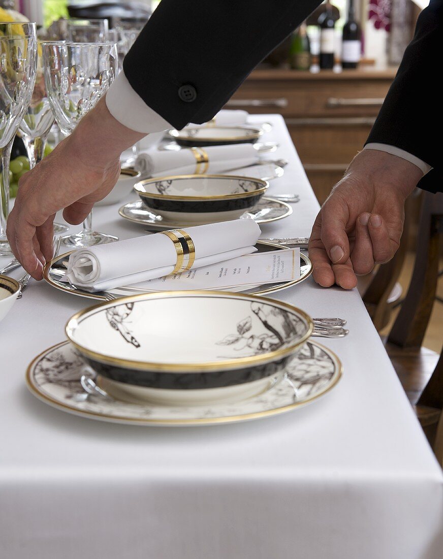 Waiter adjusting plate on table laid for special occasion