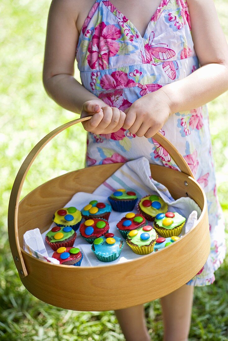 Mädchen hält Korb mit bunten Cupcakes