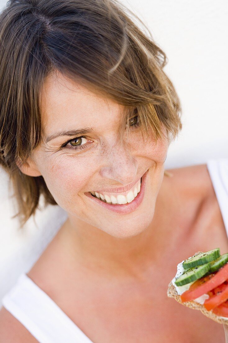 Young woman eating crispbread with soft cheese and salad