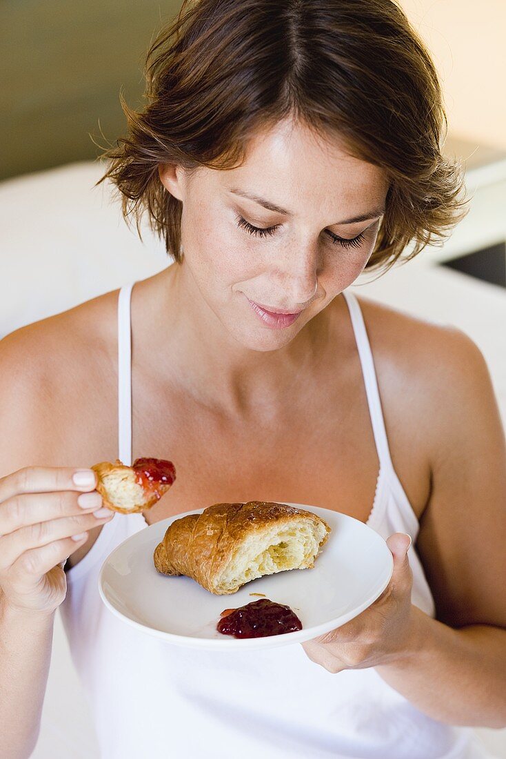 Junge Frau isst Croissant mit Marmelade