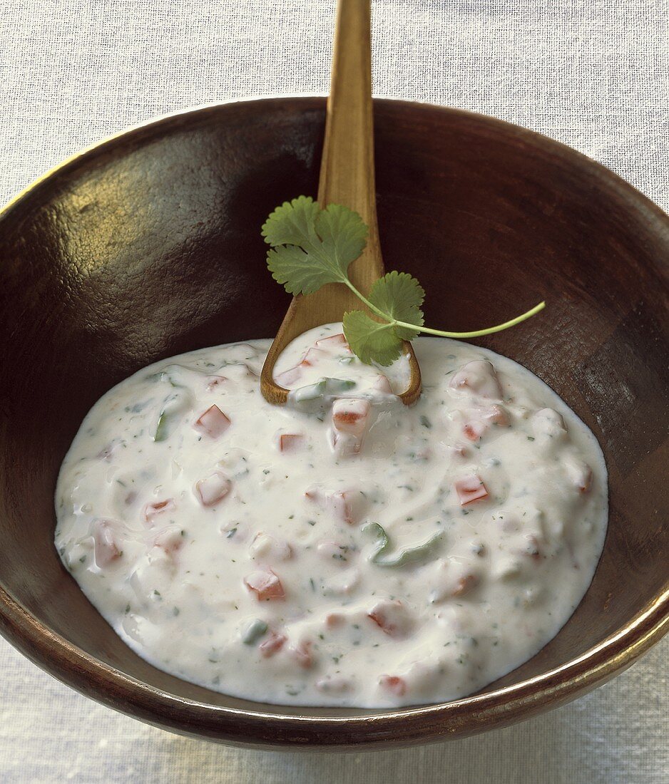 Tomato raita in a bowl with a wooden spoon