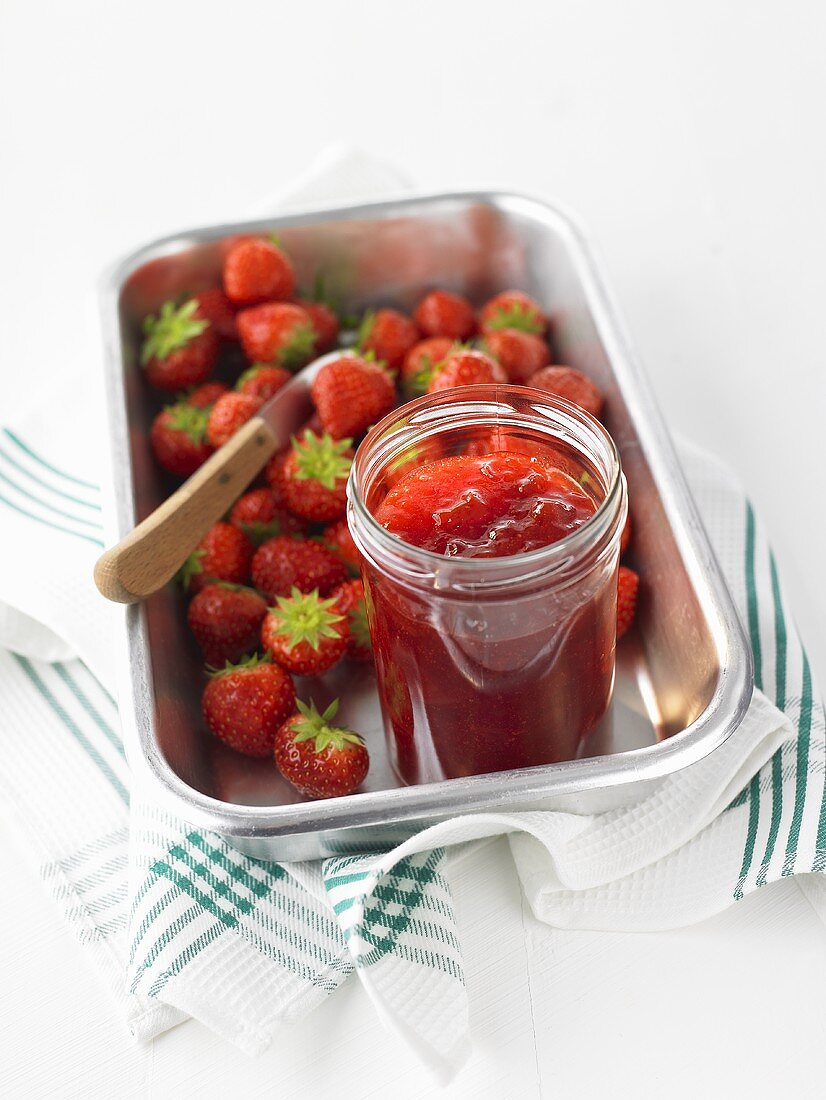 Erdbeer-Rhabarber-Marmelade im Glas, umgeben von Erdbeeren