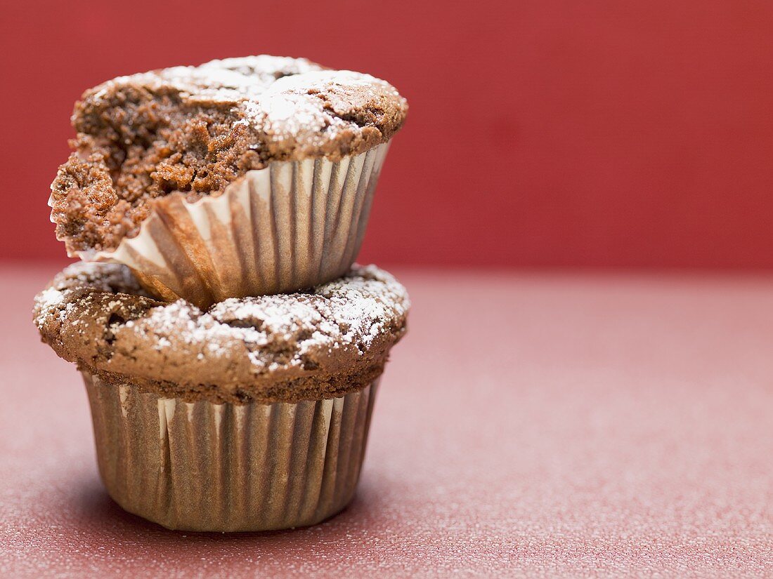 Two chocolate muffins with icing sugar, one partly eaten