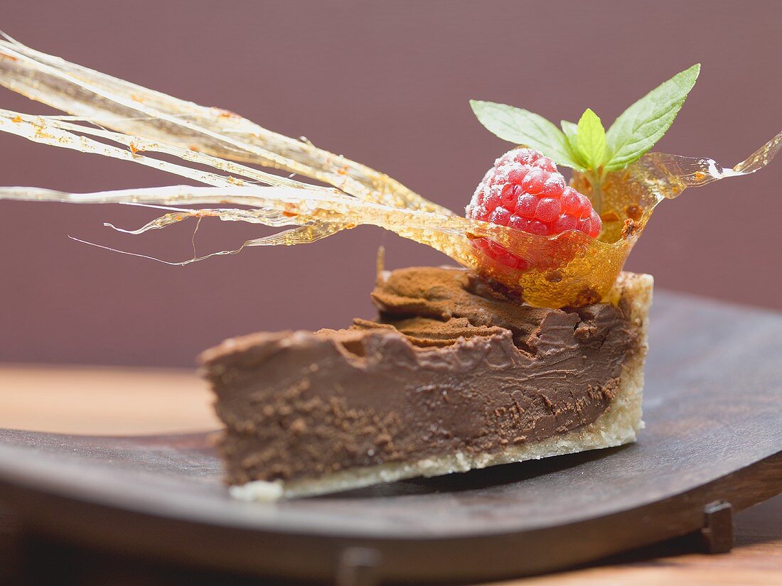 Stück Schokoladentorte mit Karamellfächer und Himbeere