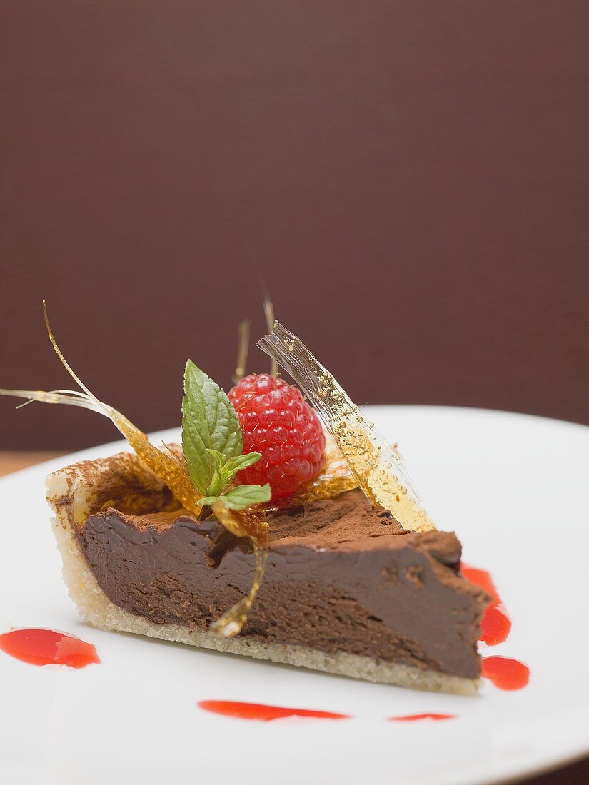 Piece of chocolate tart with a caramel fan and a raspberry