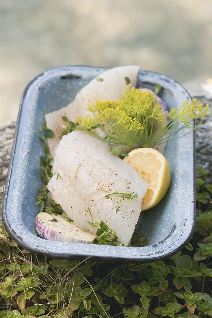 Fresh fish fillets with herbs and lemon in a dish