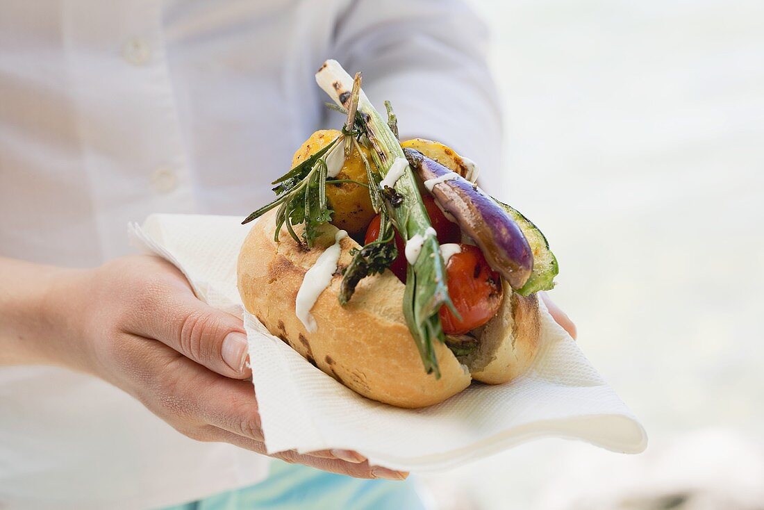 Woman holding baguette roll filled with grilled vegetables