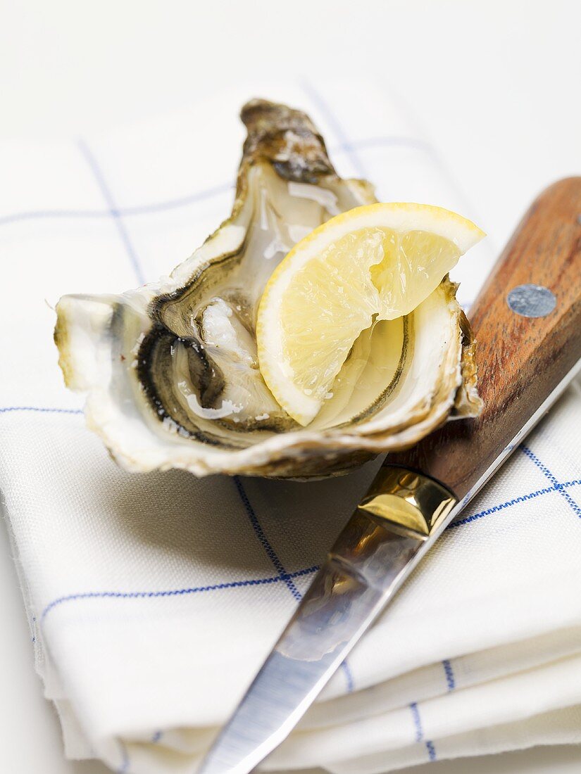 Half an oyster with lemon and knife on tea towel