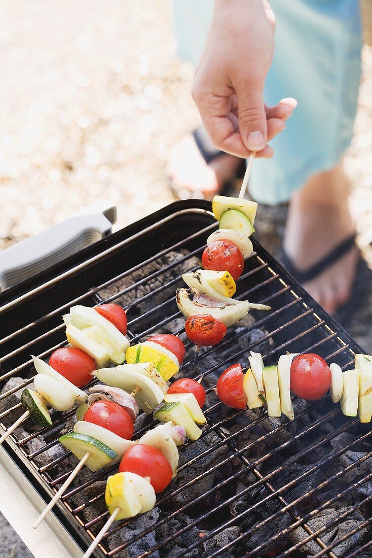Woman grilling fish and vegetable kebabs out of doors