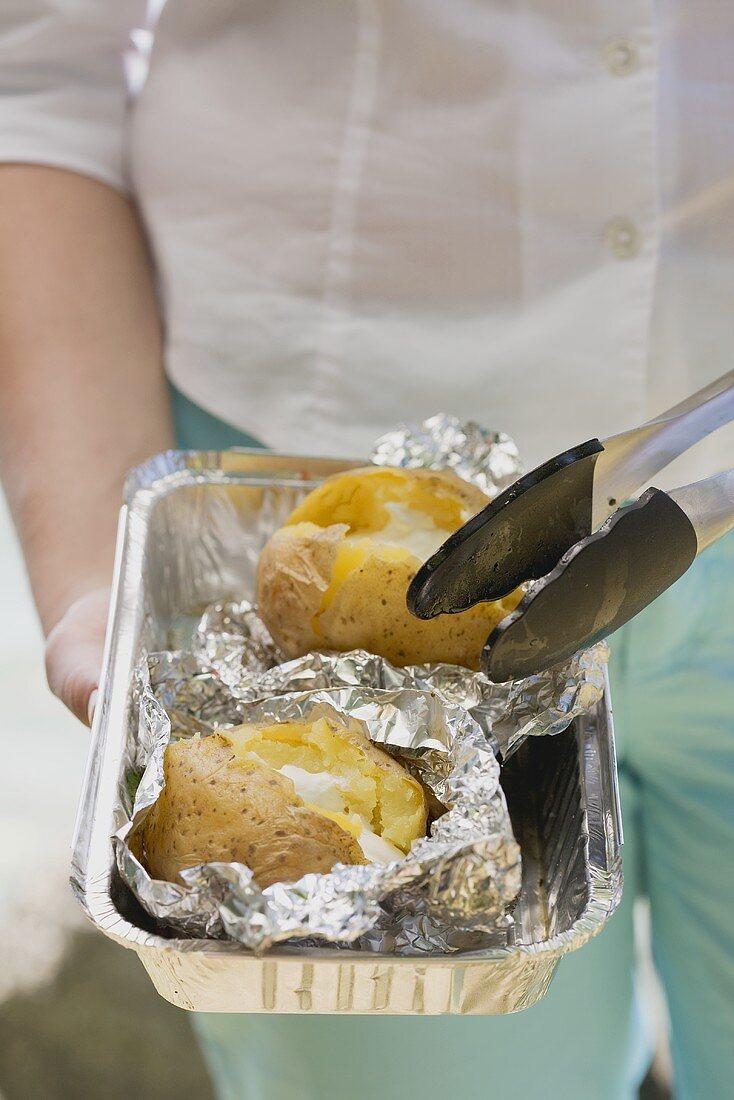 Woman holding baked potatoes in aluminium dish