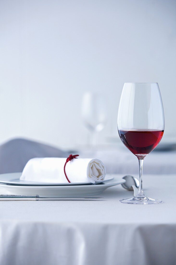 Glass of red wine on table laid in white