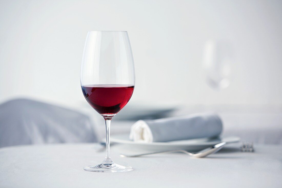 Glas Rotwein auf weiss gedecktem Tisch
