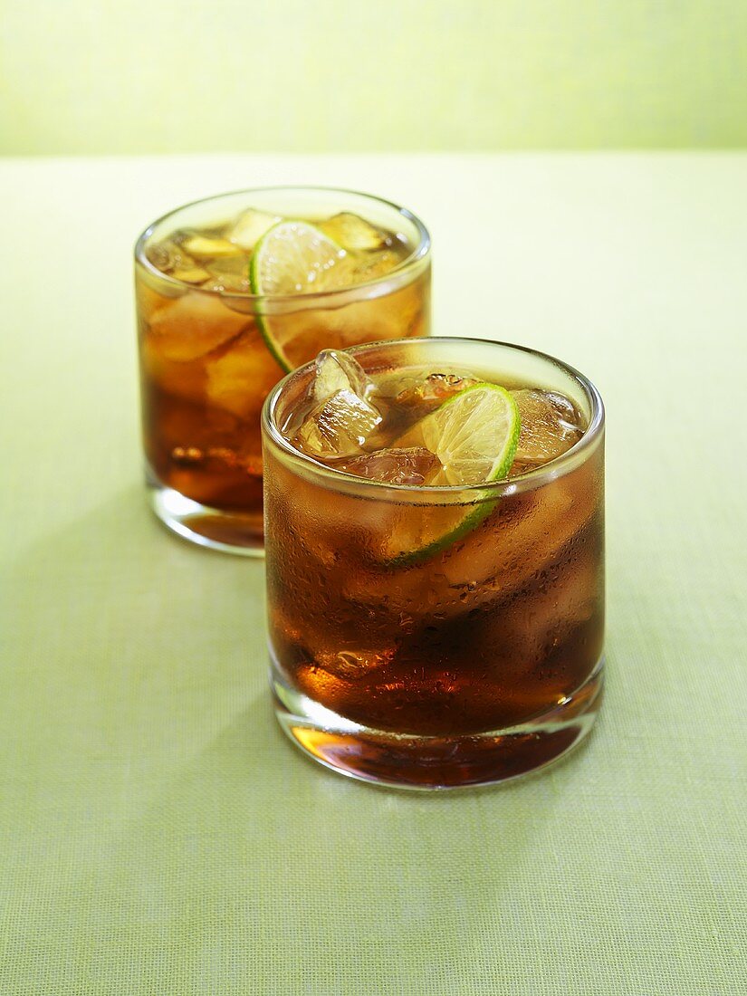 Two glasses of rum and cola with lime slices and ice cubes