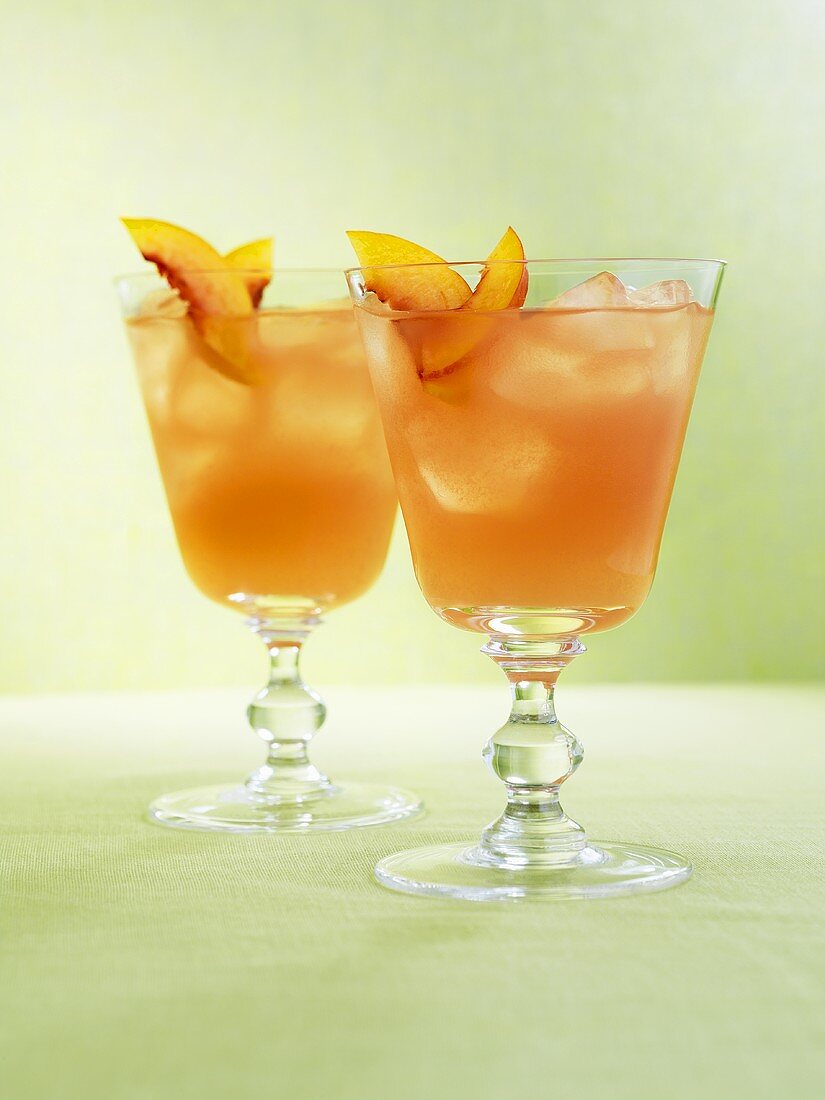 Two drinks with ice cubes and fresh peach slices