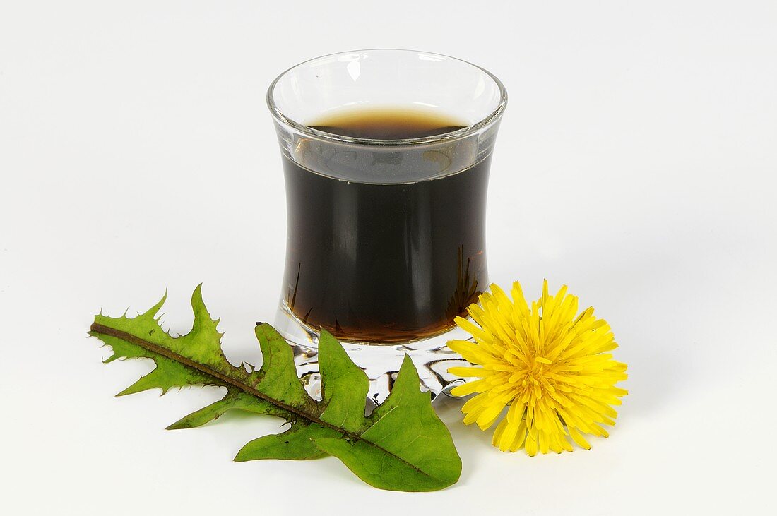 A glass of dandelion juice with flower and leaf