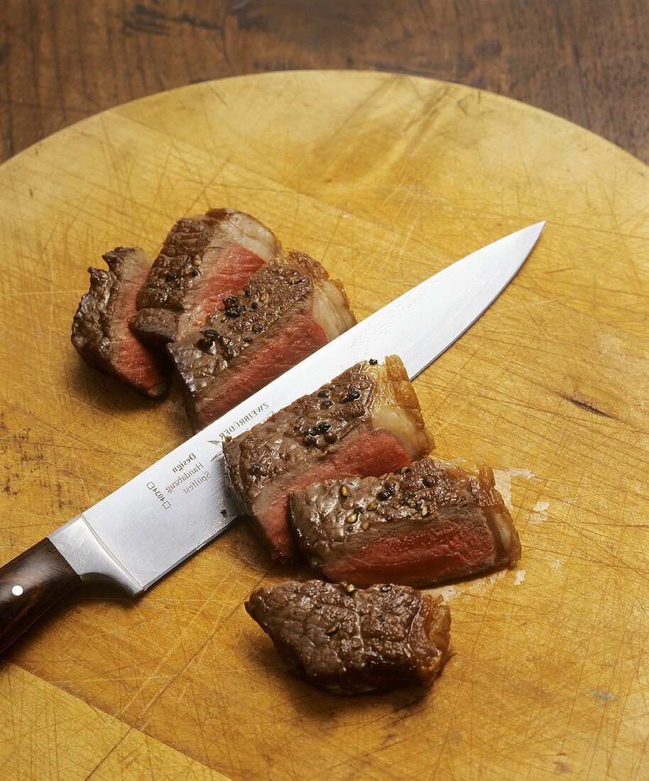Sliced roast beef on wooden board with knife