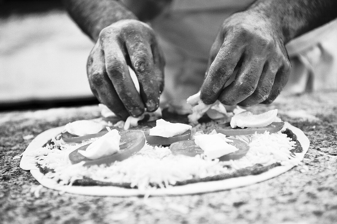 A pizza maker covering a pizza with mozzarella