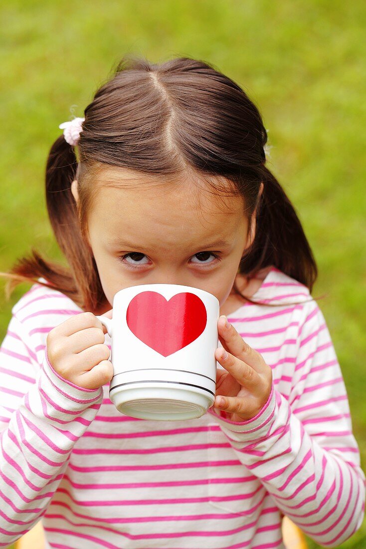 A girl drinking tea from a mug with a heart