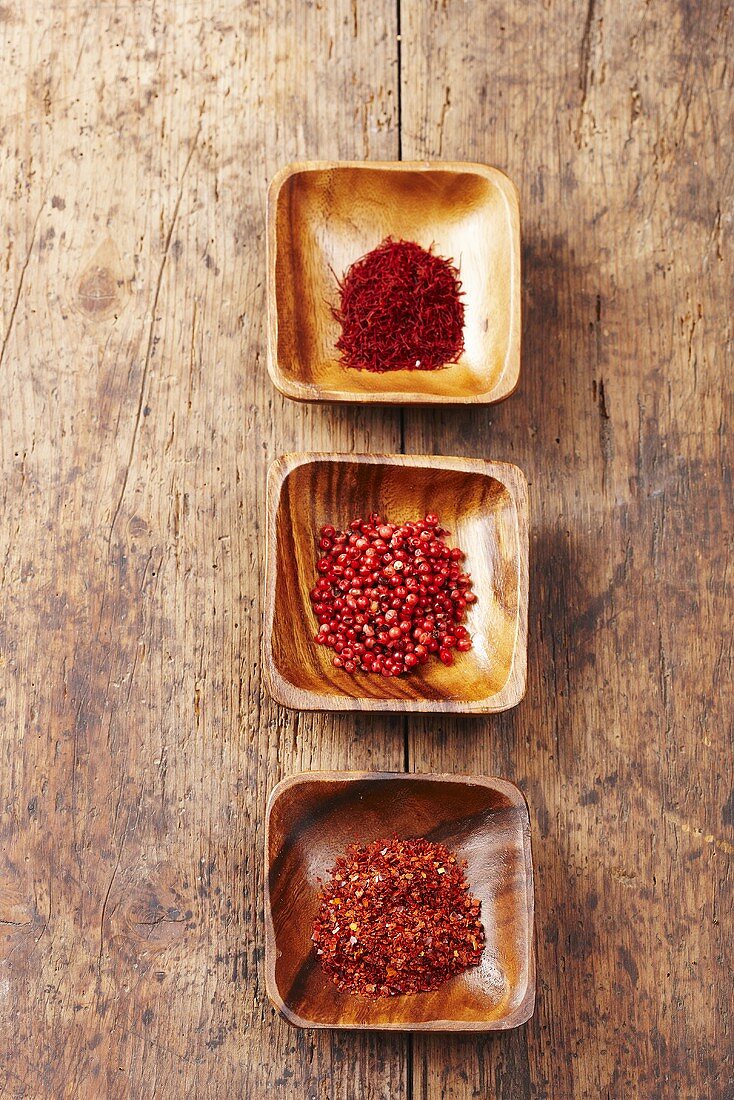 Chilli flakes, pink peppercorns and saffron threads in wooden bowls