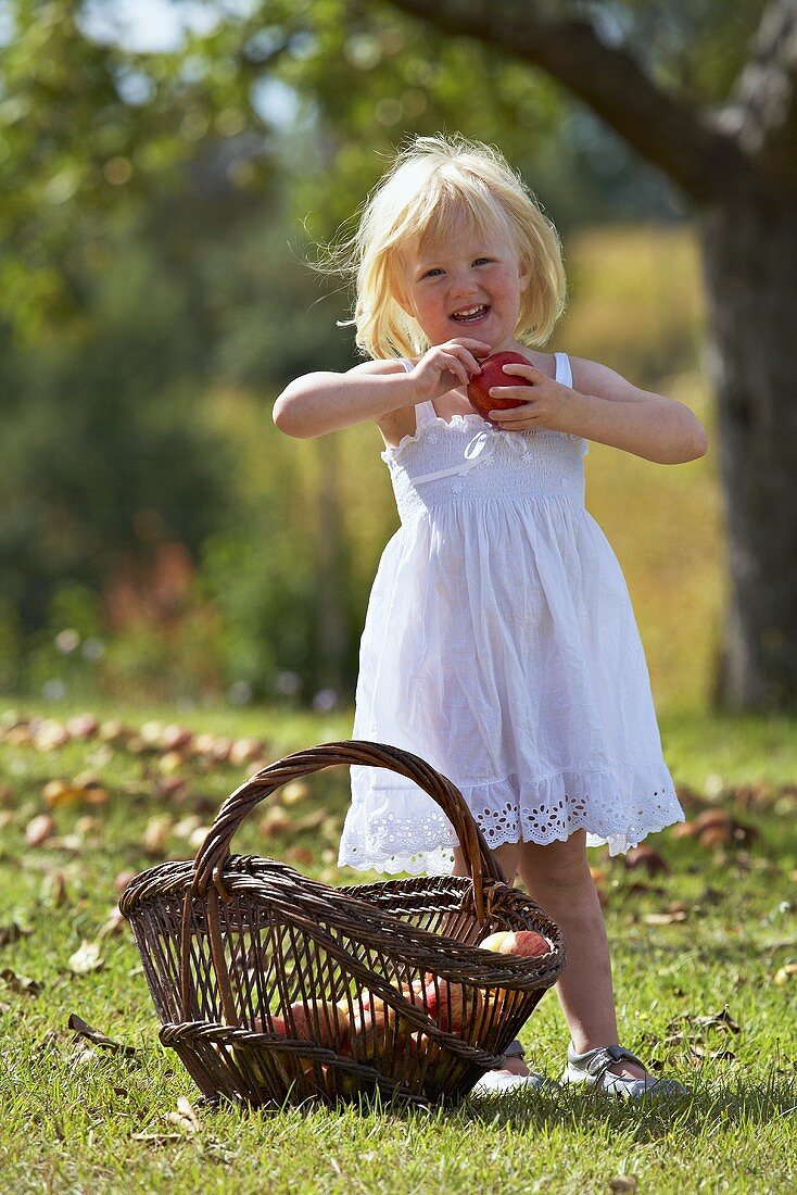 A blonde girl in a garden holding an apple