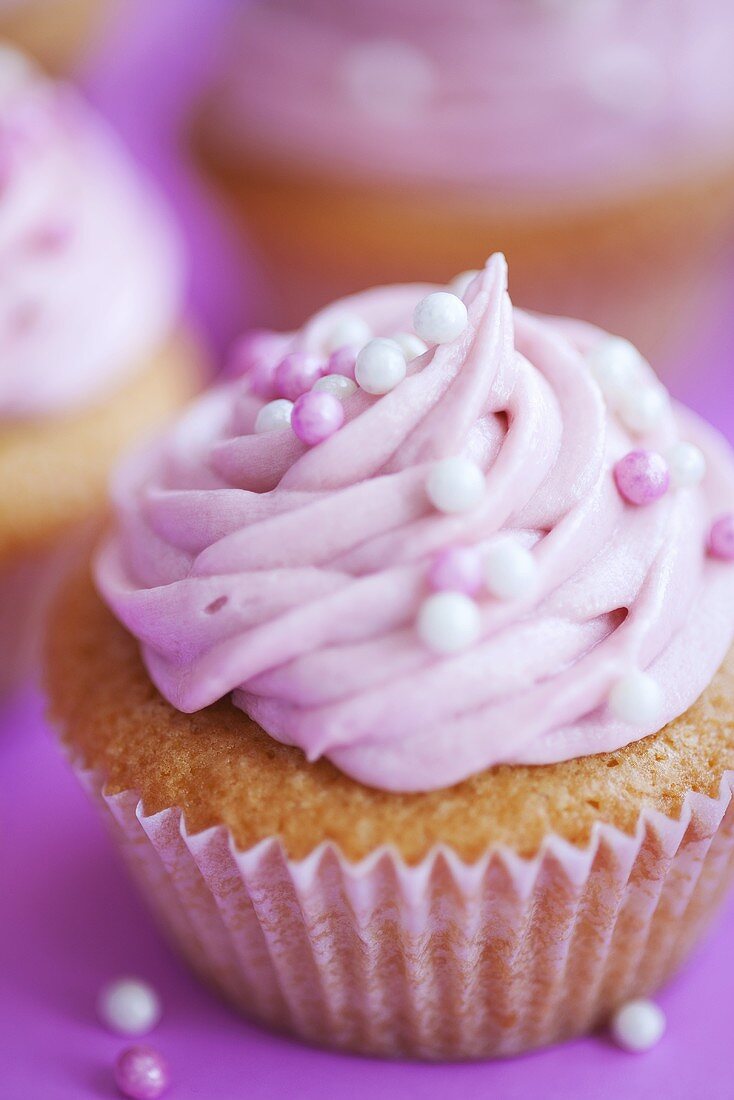 A cupcake decorated with pink cream and sugar balls
