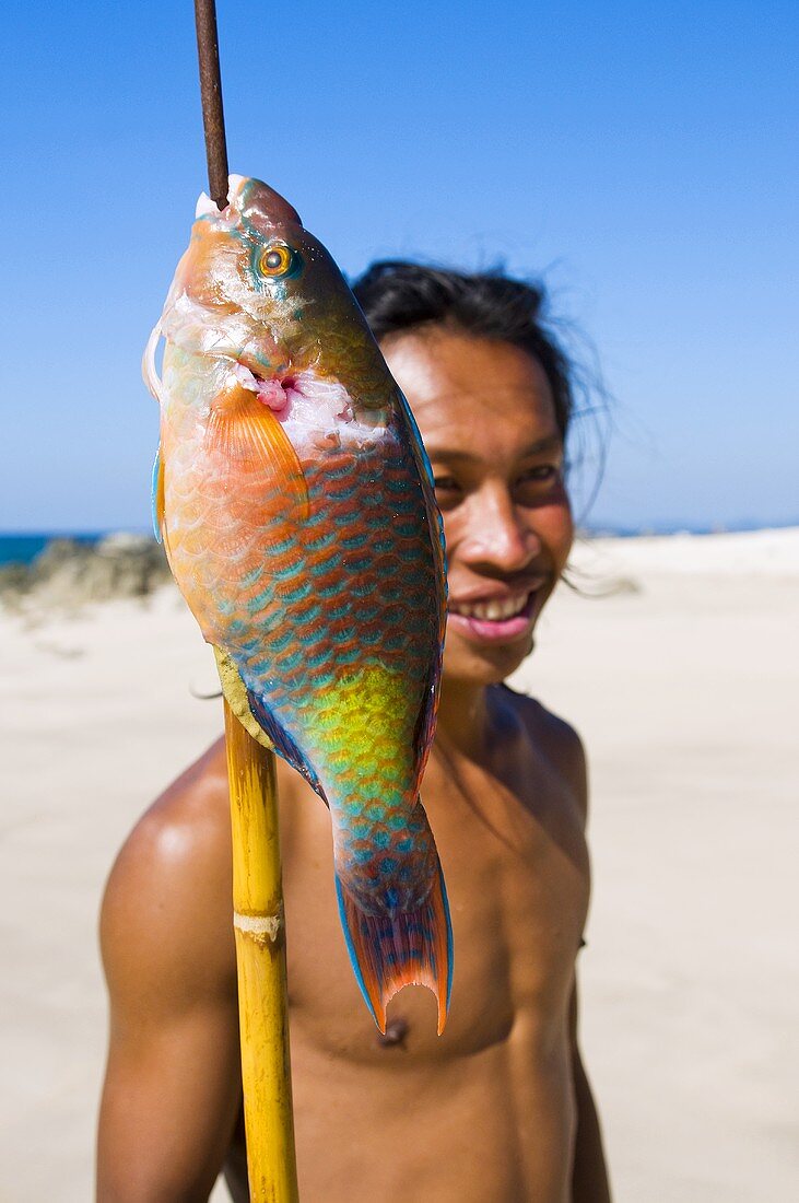 A young man with a speared parrotfish on a beach