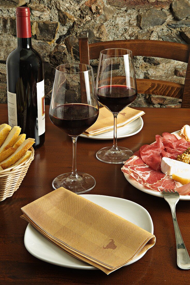 A plate of sliced meats with cheese and red wine