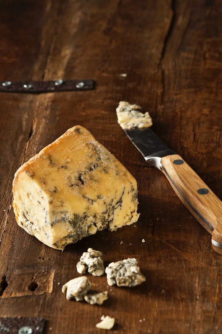 A piece of Stilton with a knife on a wooden surface