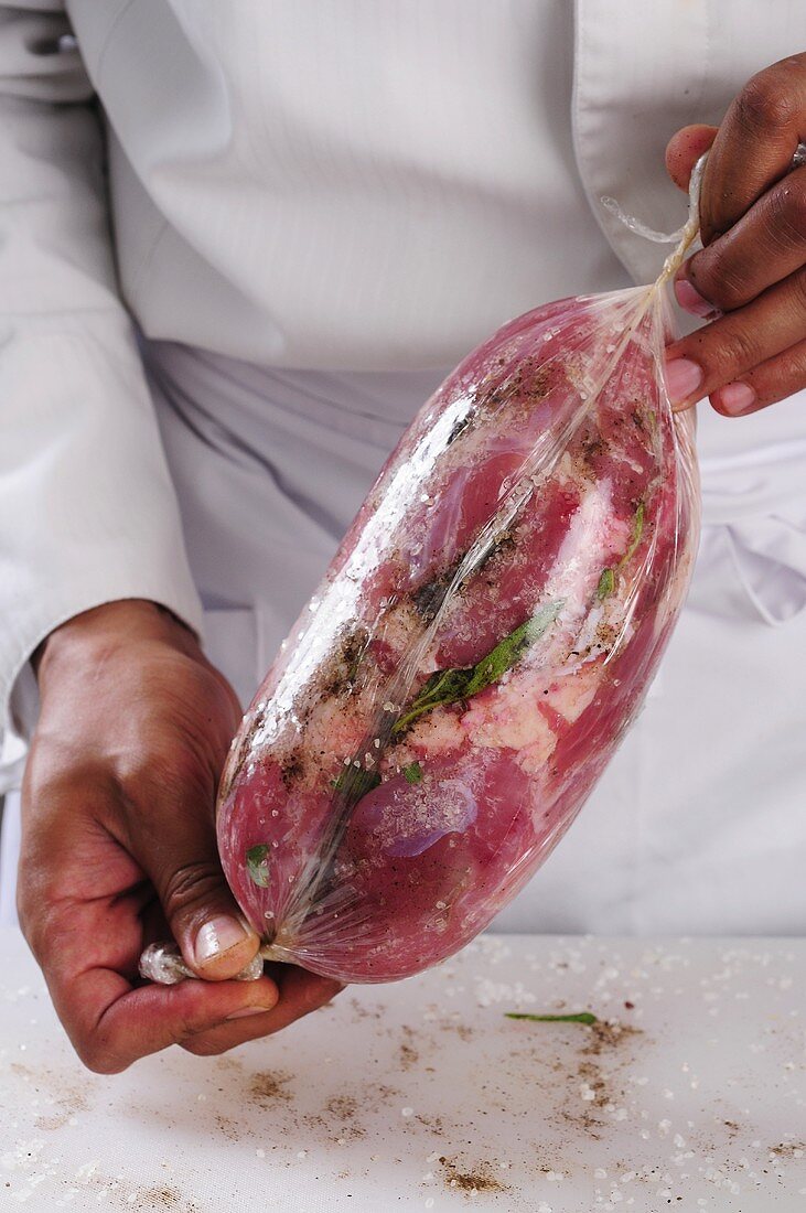 A pork shoulder joint being wrapped in clingfilm
